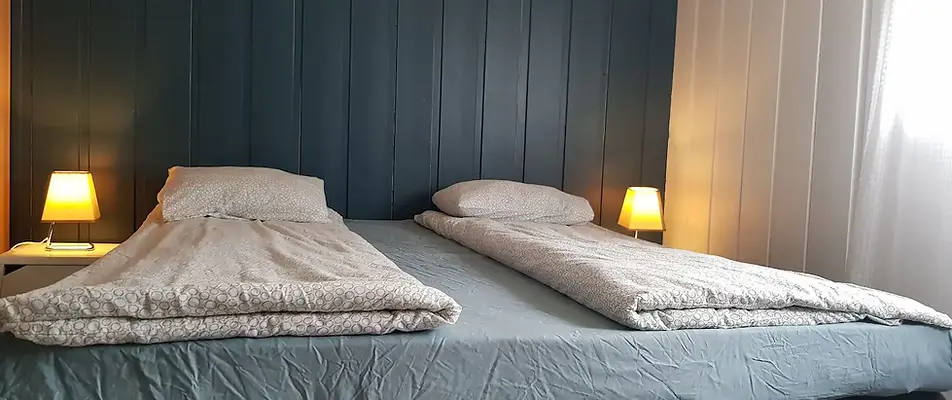 Cozy bedroom with two single beds placed together, soft lighting from bedside lamps, and a dark blue accent wall.