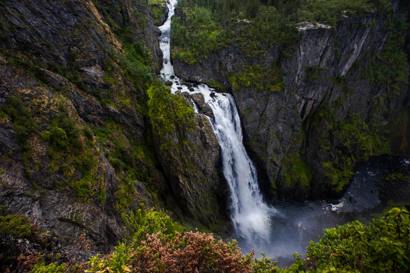 Spektakulær foss omgitt av bratte fjellsider med grønn vegetasjon.