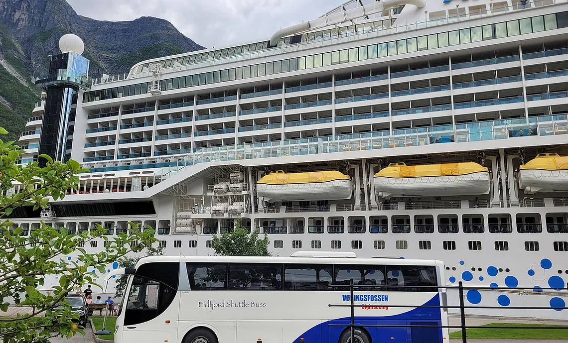 Eidfjord Shuttle Bus parked in front of a large cruise ship named 'AIDA' in the harbor.