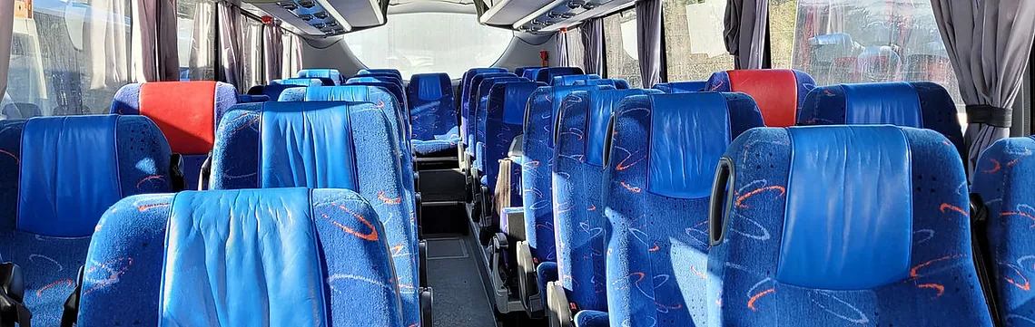 Interior of a tour bus with rows of blue seats and large windows, ready to welcome passengers.